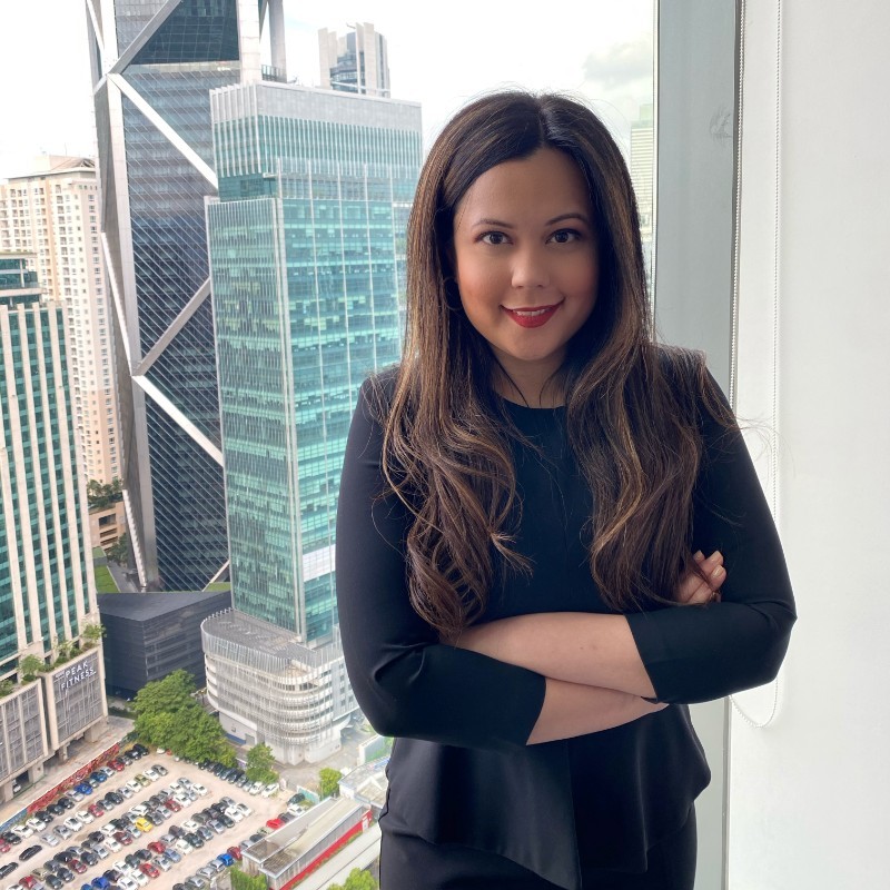 Woman smiling with arms crossed in an office with skyscrapers in the background.