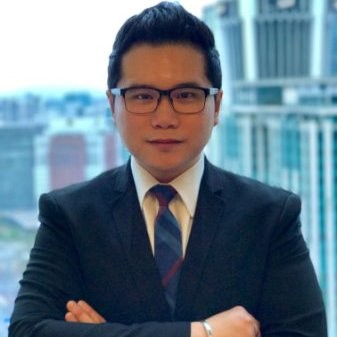 Person in glasses and suit posing in front of cityscape.