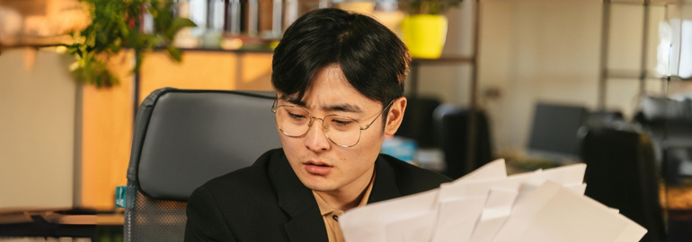 A man wearing glasses looks anxiously at a job counter-offer letter, contemplating his next move.