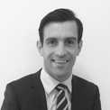 Black and white photo of a man in a suit and tie, smiling.