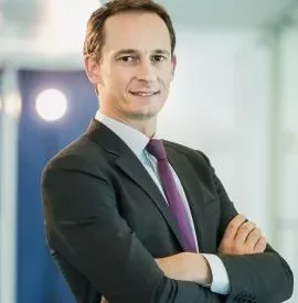 Confident individual in a suit with arms crossed in an office setting.