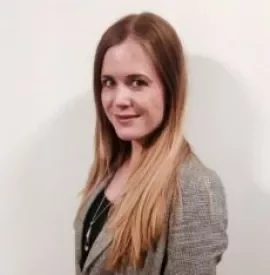 Portrait of a woman with long hair wearing a gray blazer, smiling slightly at the camera.