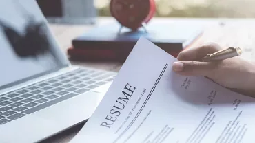 Person holding a resume in front of a laptop.