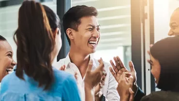 Group of diverse colleagues laughing and clapping in an office.