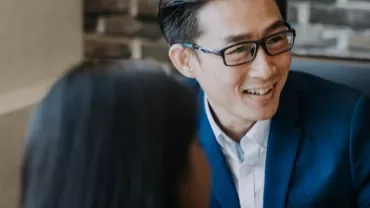 A man in a blue suit and glasses smiles during a meeting.