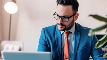 Man in blue suit working on a laptop in a modern office.