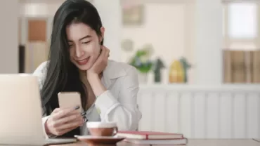 Woman smiling at her phone with a laptop and coffee on the table