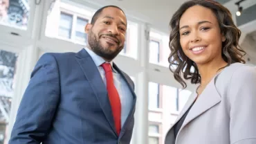 Two people smiling in a modern office with large windows.