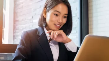 Businesswoman smiling and using a laptop at a desk.