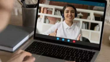 A person on a video call giving a thumbs-up, visible on a laptop screen.