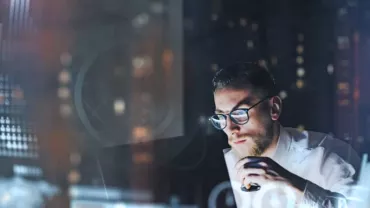 Man in glasses analyzing digital data with graphs around him.