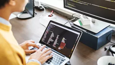 Person coding on a laptop with additional screen nearby.