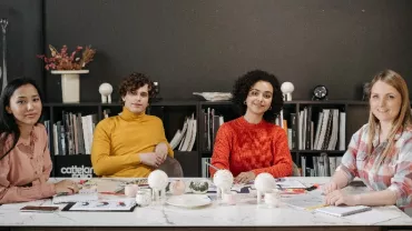 Four people sitting at a table in an office, surrounded by books and decor.