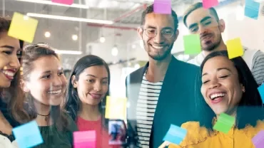 Group of diverse people brainstorming with sticky notes on glass.