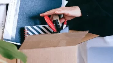 Person packing office supplies into a cardboard box.