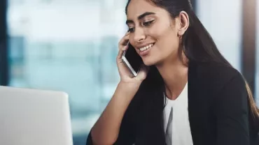 Woman smiling while talking on the phone at a laptop.