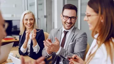 Group of professionals clapping and smiling in a meeting room.