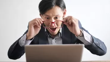 Man with red glasses looking surprised at a laptop screen.