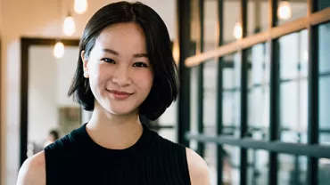 Woman with short hair smiling in a modern office with glass walls.