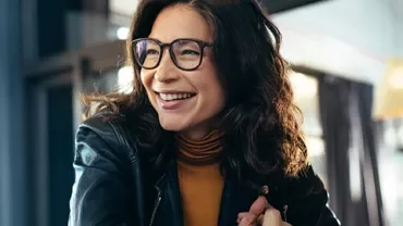 Woman in glasses smiling inside a cafe.