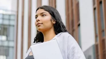 Woman holding a laptop in front of a modern building.