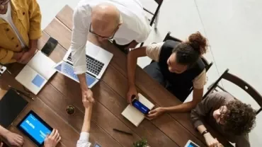 A group of professionals engaged in leadership networking, sitting around a table with laptops and tablets