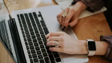 A woman typing on a laptop, wearing a watch on her wrist, focused on her work.