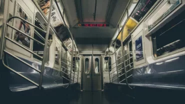 Empty subway car interior with metal poles and overhead advertisements.