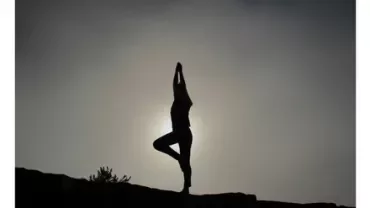 Silhouette of a person doing yoga tree pose at sunset.