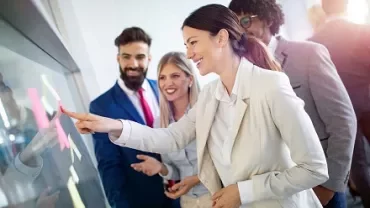 Team collaborating at an office meeting with sticky notes on a glass board.