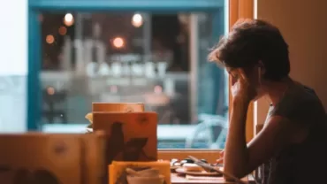 Person with earphones sitting by a cafe window, surrounded by books.