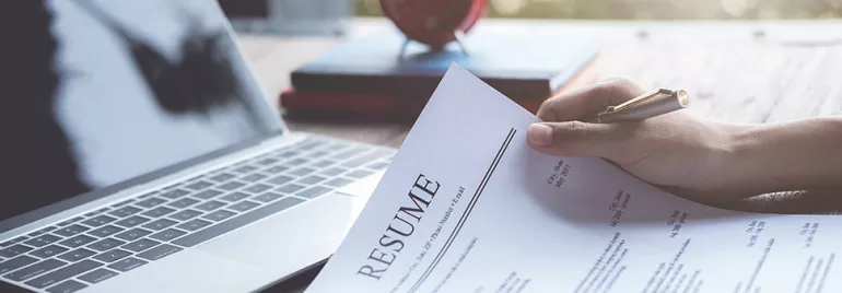 Person holding a resume in front of a laptop.