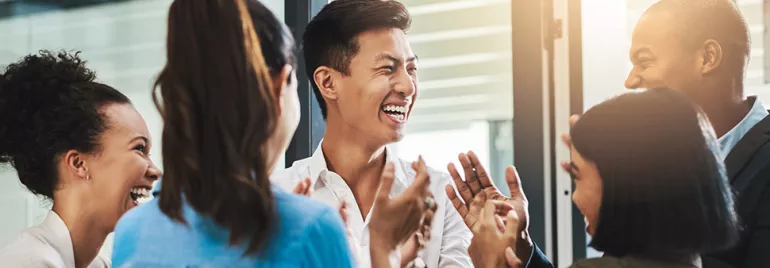 Group of diverse colleagues laughing and clapping in an office.