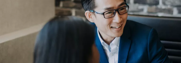 A man in a blue suit and glasses smiles during a meeting.