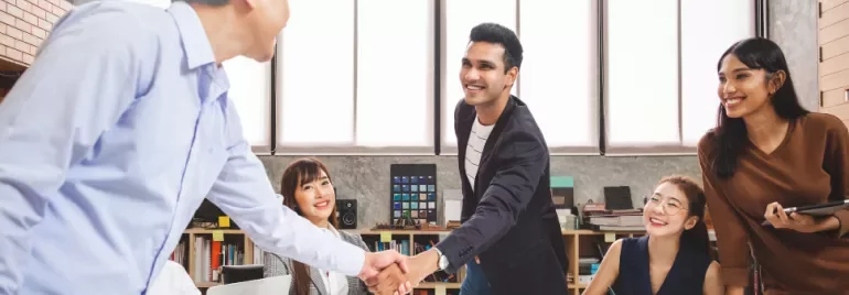 Team members smiling as two men shake hands in a modern office.