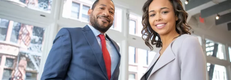 Two people smiling in a modern office with large windows.