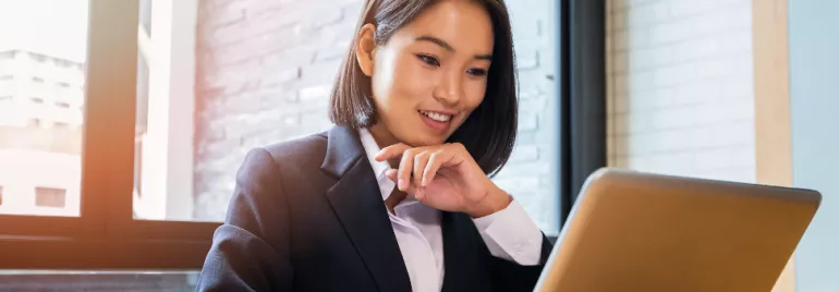 Businesswoman smiling and using a laptop at a desk.