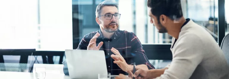 Two men having a discussion at a table with a laptop.
