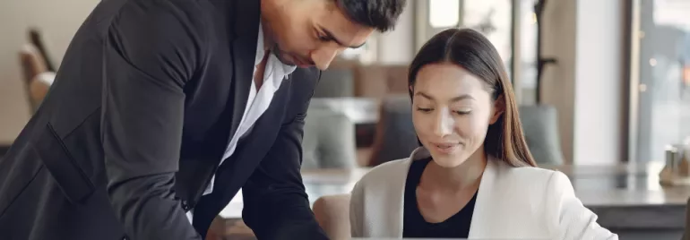 Two colleagues engaged in a discussion over a laptop in an office setting.