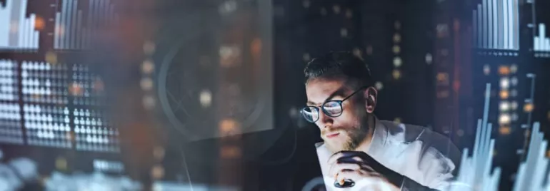 Man in glasses analyzing digital data with graphs around him.