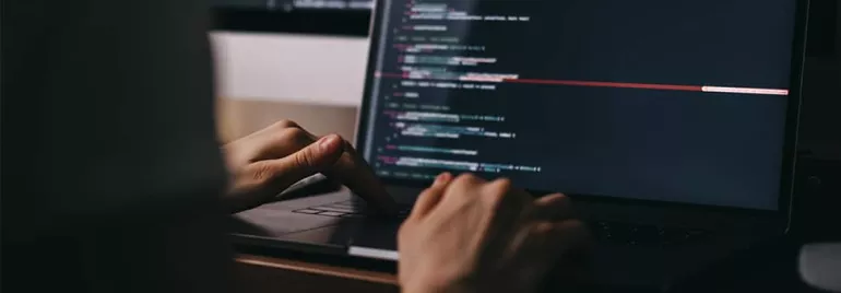Hands typing code on a laptop keyboard.