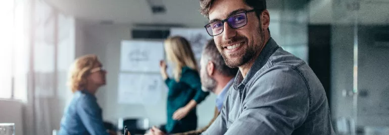 Smiling man with glasses in a meeting room with colleagues.