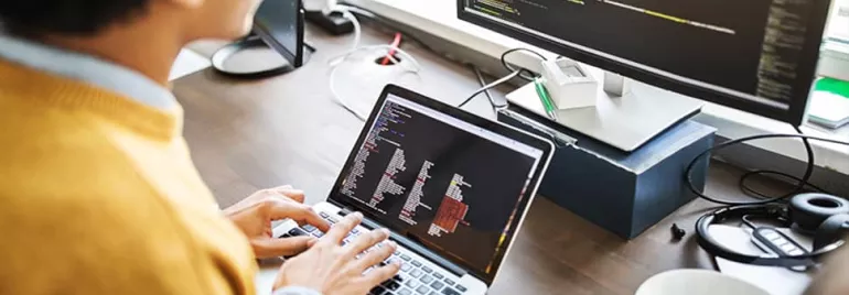 Person coding on a laptop with additional screen nearby.