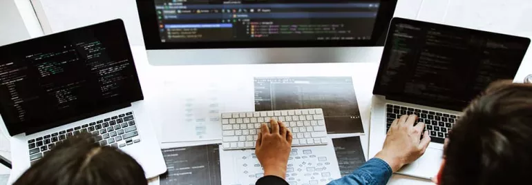 People working on laptops with code on screens, collaborating around a desk.
