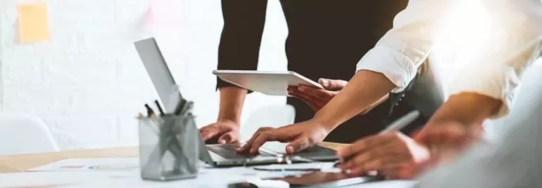 People collaborating at a desk with laptops and tablet.