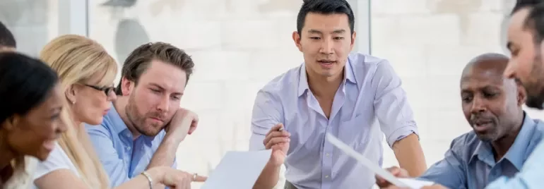 A diverse group of people in a meeting, discussing documents around a table.