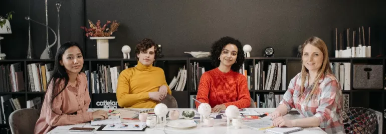 Four people sitting at a table in an office, surrounded by books and decor.