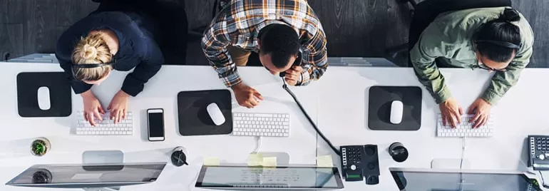 Overhead view of three people working at desks with computers and phones.
