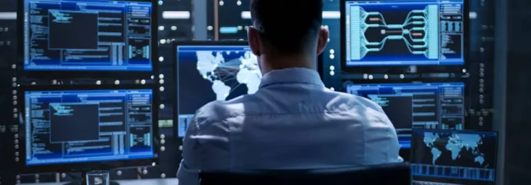 Person in front of multiple monitors displaying data and maps in a control room.