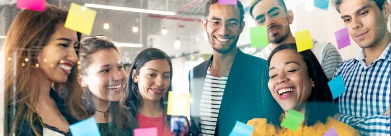 Group of diverse people brainstorming with sticky notes on glass.